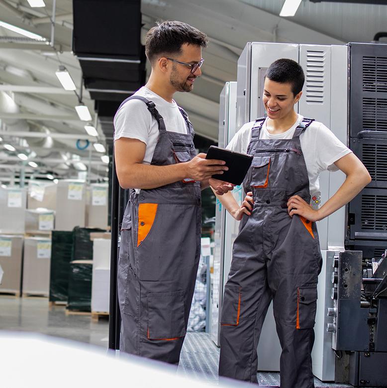 Zwei Elektrofachkräfte besprechen technische Unterlagen in Industriehalle